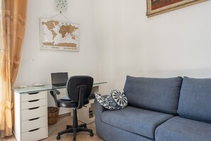 A room with a glass desk, a black office chair, a blue sofa, a world map on the wall, and a lamp on the desk. - Apartment 'Mondello Holidays - Casa Neruda' with Sea View, Wi-Fi and Air Conditioning (Palermo)