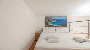 A bedroom with a bed, a nightstand, a lamp, and a painting of a coastal landscape.