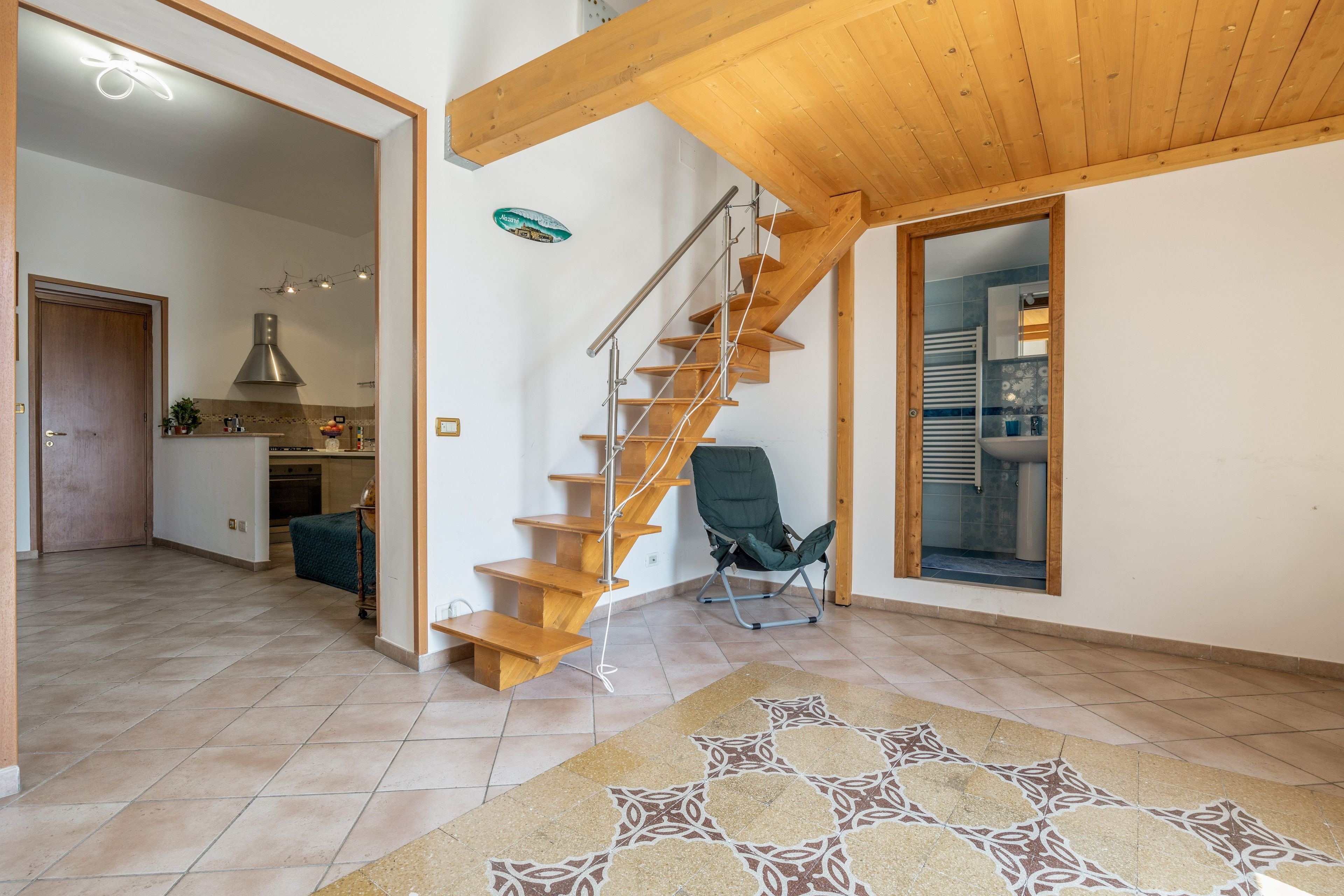 Een ruime woonkamer met een houten trap, een eethoek en een zicht op een andere kamer.