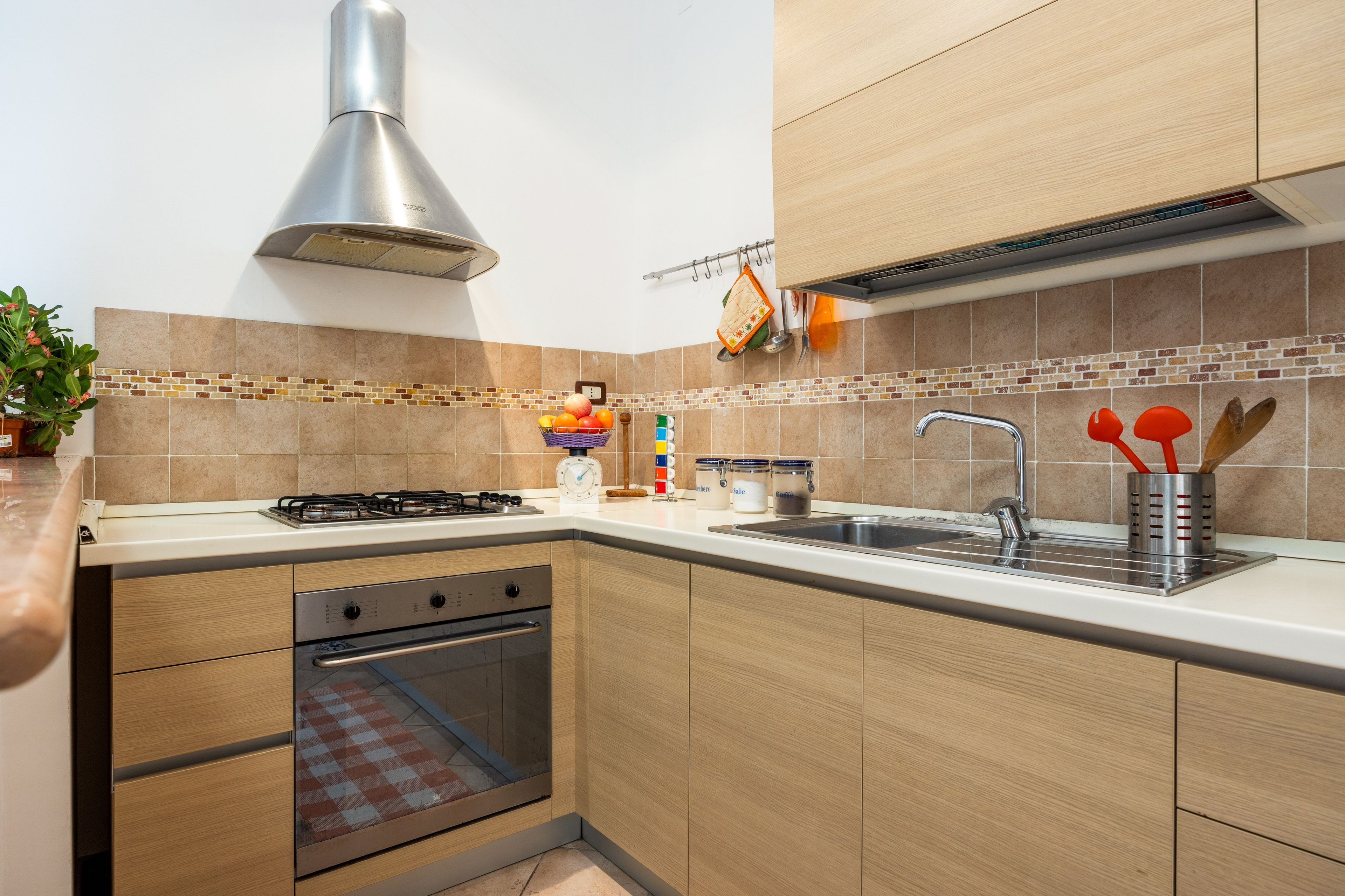 Een moderne keuken met een gasfornuis, oven, een roestvrijstalen spoelbak en houten keukenkastjes.