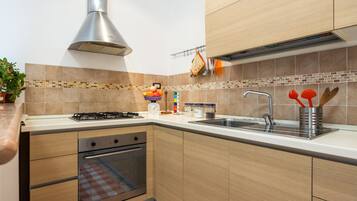 Een moderne keuken met een gasfornuis, oven, een roestvrijstalen spoelbak en houten keukenkastjes.