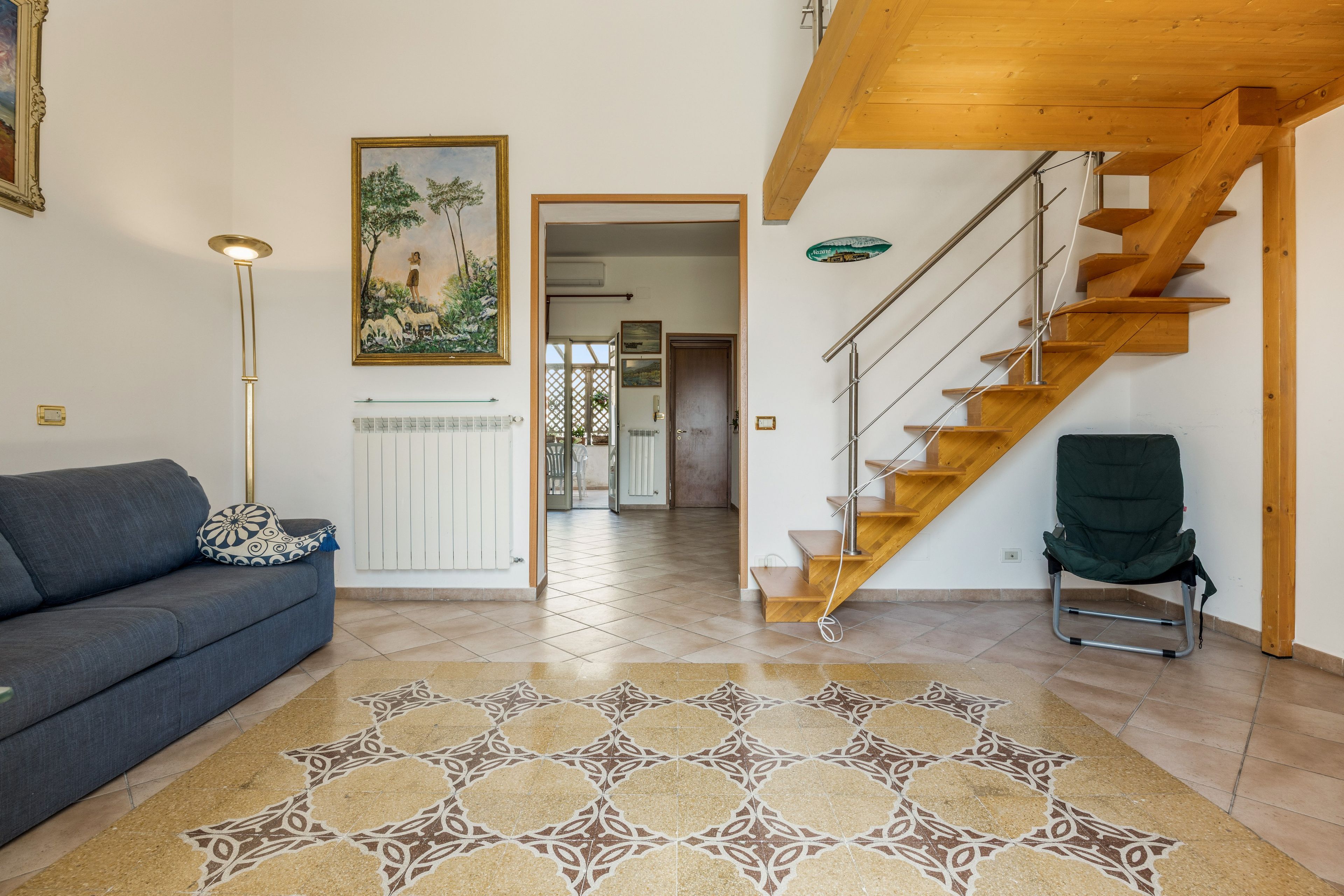 Un salon avec un canapé, un tapis à motifs, un tableau et un escalier en bois.