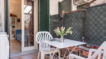 A patio area with a table and chairs, a small vase with flowers, and a view of the interior through a glass door.