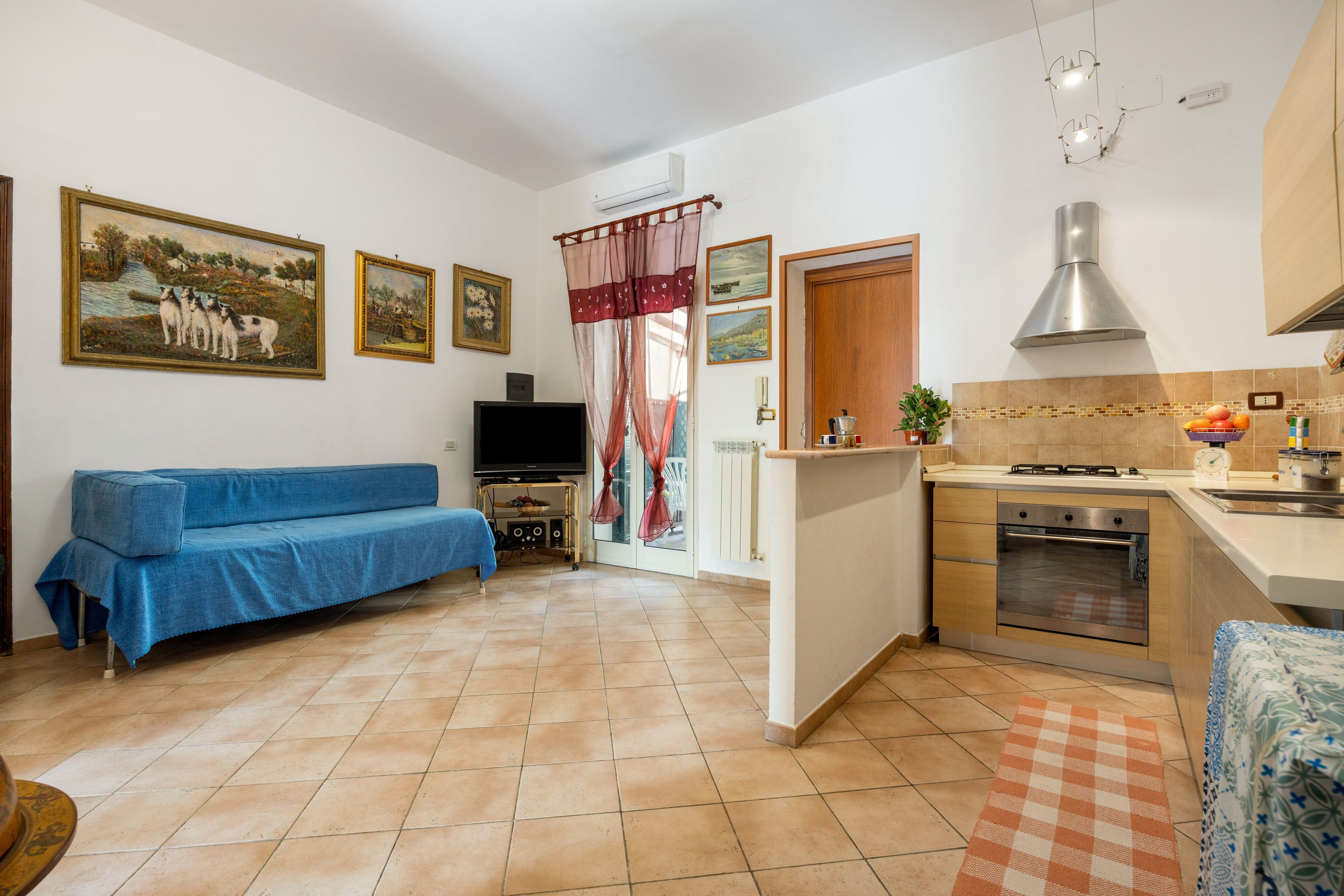 A compact living space with a sofa, a television, a kitchen area with a stove and oven, and a dining table.