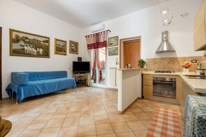 A compact living space with a sofa, a television, a kitchen area with a stove and oven, and a dining table. - Apartment 'Mondello Holidays - Casa Neruda' with Sea View, Wi-Fi and Air Conditioning (Palermo)