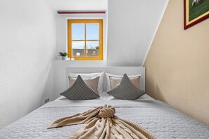 A bedroom with a bed, pillows, a blanket, a window, and a plant. - Modern beachfront apartment with exceptional sea views at Schönberger Strand (Schönberg (Holstein))