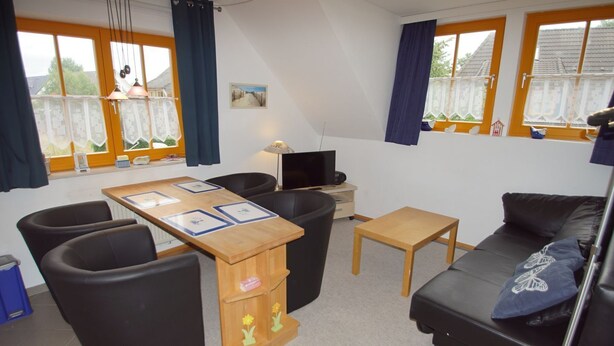 Een gemeubileerde woonkamer met een bank, stoelen, een kleine tafel, een televisie en een raam met gordijnen.