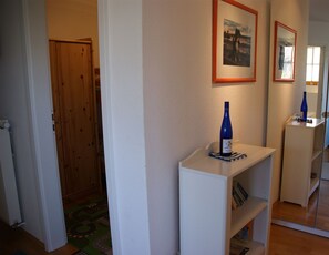 A hallway with a wooden door, a white shelf with a bottle, and framed pictures on the wall. - Modern beachfront apartment with exceptional sea views at Schönberger Strand (Schönberg (Holstein))