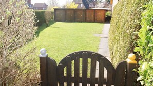 Een woonhuis met een verzorgd gazon, een houten poort en een bakstenen gebouw op de achtergrond.
