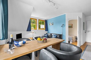 A modern room with a wooden dining table, black leather chairs, a blue accent wall, and a view through a window with curtains. - Modern beachfront apartment with exceptional sea views at Schönberger Strand (Schönberg (Holstein))