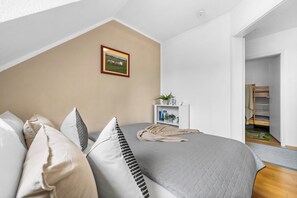 A bedroom with a bed, pillows, a bedside table with a plant, and a framed picture on the wall. - Modern beachfront apartment with exceptional sea views at Schönberger Strand (Schönberg (Holstein))