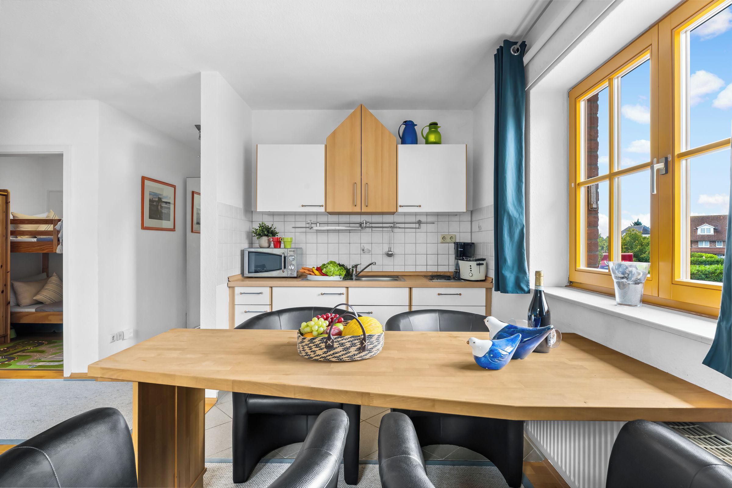 Eine moderne Küche mit weißen Schränken, einer Mikrowelle und einem Essbereich mit Holztisch und Stühlen.
