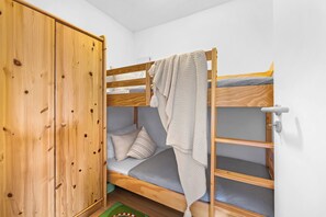 Een stapelbed met een houten frame, een groene mat bij het voeteneinde en een garderobe met houten afwerking.
