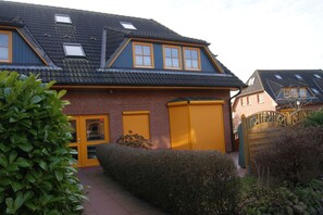 A residential house with a sloped roof, dormer windows, and a garage with yellow shutters. - Modern beachfront apartment with exceptional sea views at Schönberger Strand (Schönberg (Holstein))
