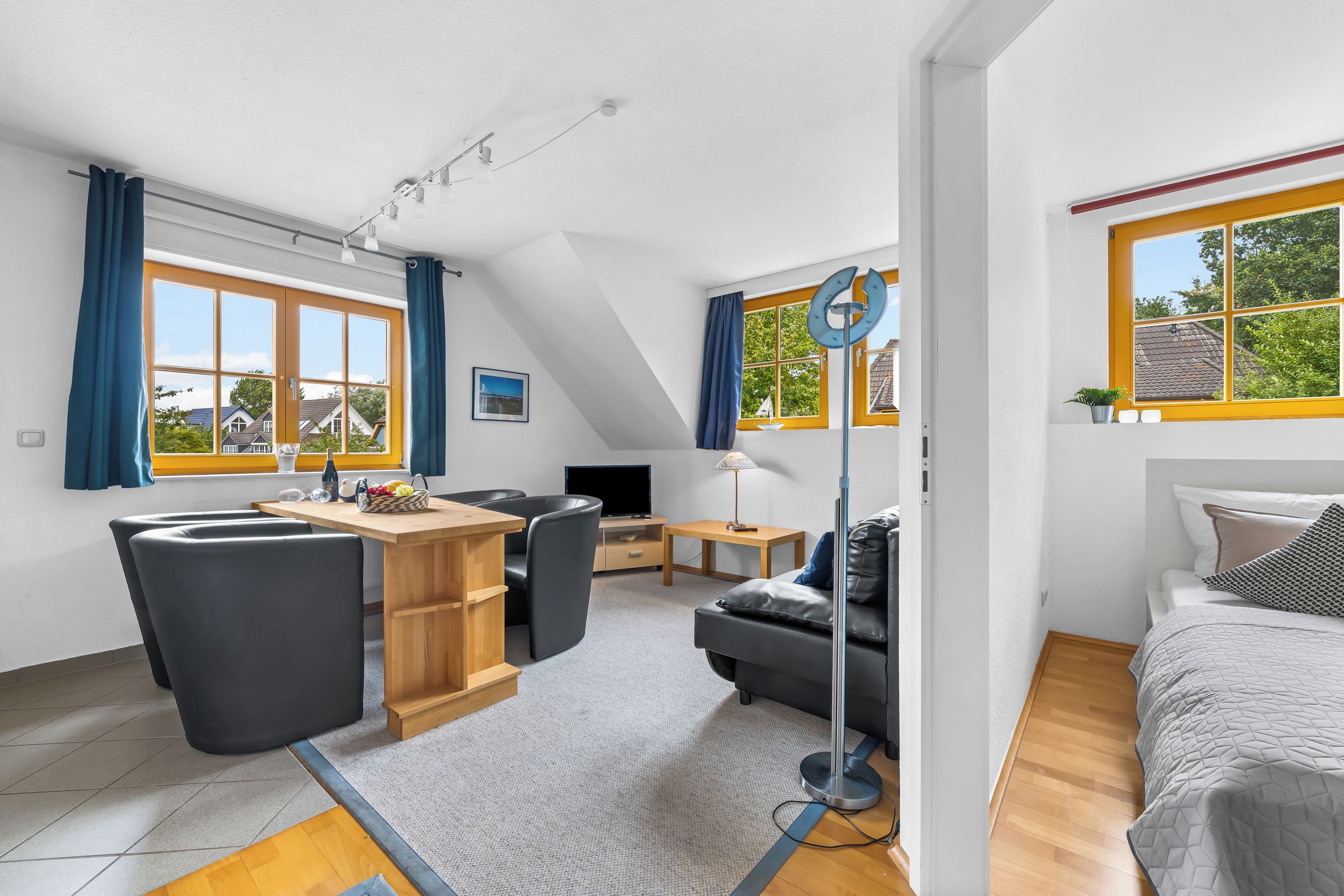 Een moderne, goed verlichte kamer met een eethoek, een bank, een bed en grote ramen met uitzicht.