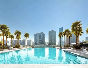 A swimming pool with lounge chairs and palm trees, surrounded by high-rise buildings. - StayShort - Studio in Business Bay Balcony that Sleeps 2 (Business Bay)