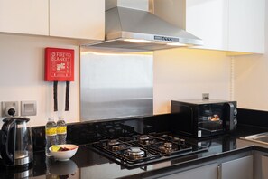 A modern kitchen with a stainless steel range, a Bosch hood, a black coffee maker, and a red fire blanket on the wall. - StayShort - Studio in Business Bay Balcony that Sleeps 2 (Business Bay)