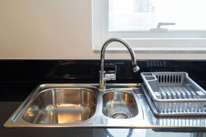 A stainless steel kitchen sink with a faucet, a dish rack, and a window in the background. - StayShort - Studio in Business Bay Balcony that Sleeps 2 (Business Bay)