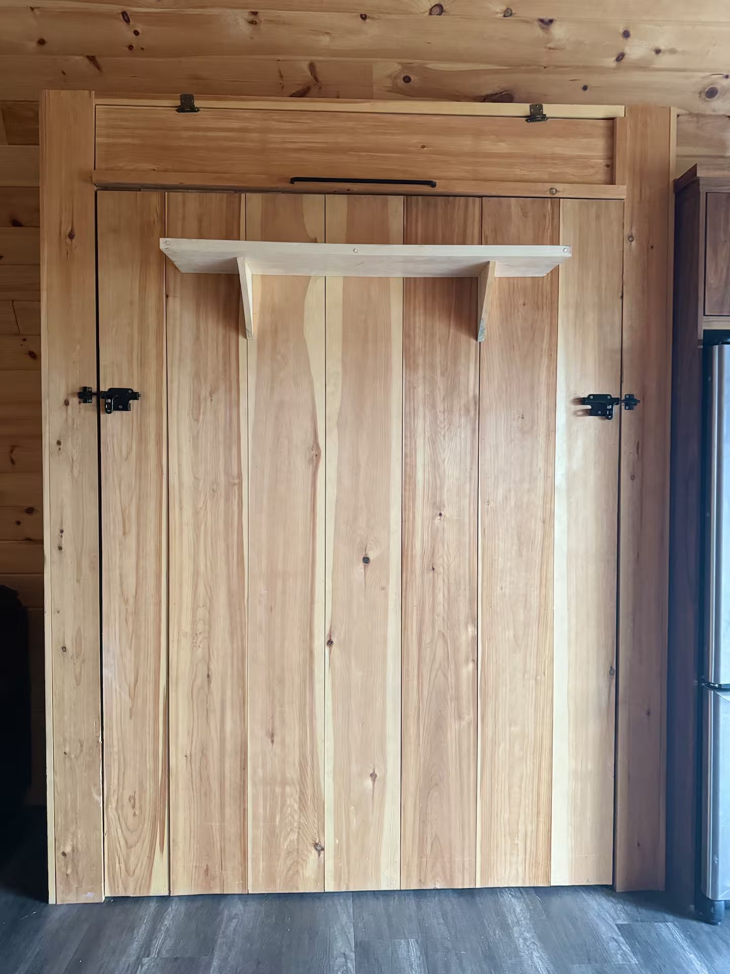 Une porte en bois avec une poignée en métal et une étagère au-dessus.