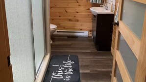 Passadís estret que condueix a un bany amb vàter, rentapans i finestra.