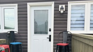 A wooden deck with a white door, two chairs, and a small table.