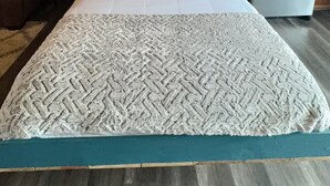 Habitació d'una cabana de fusta amb un llit, almoines, un frigorífic i una paret blava.