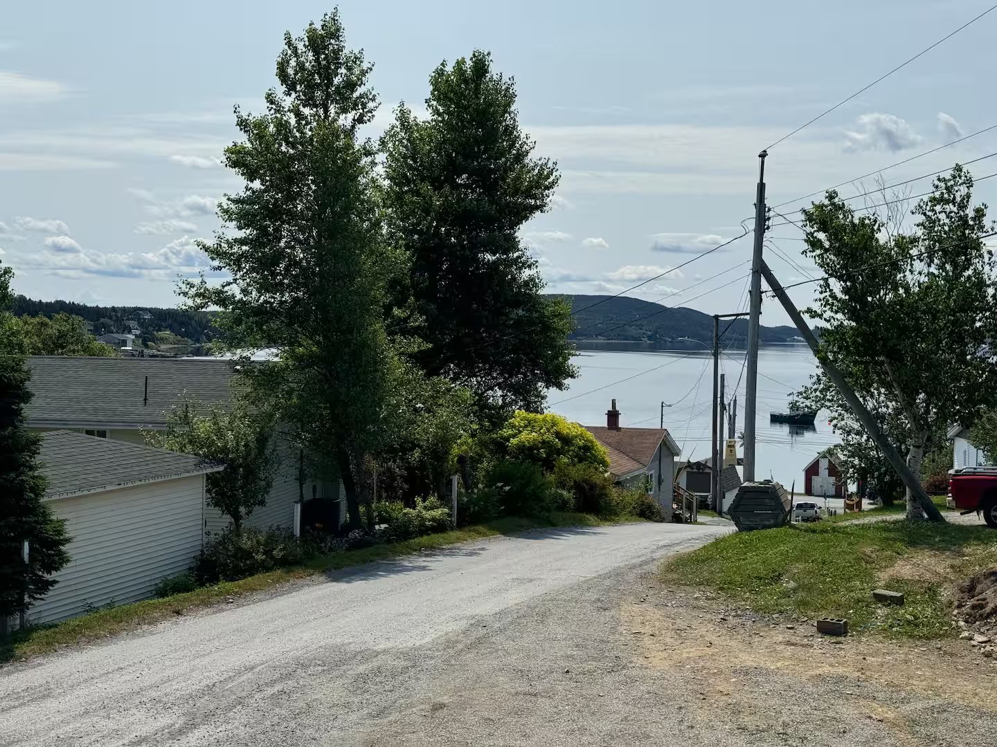 Un camino de grava que conduce a una zona residencial con casas, un muelle y una masa de agua al fondo.