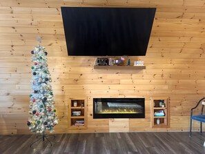 A living room with a fireplace, a television mounted on the wall, and a Christmas tree.