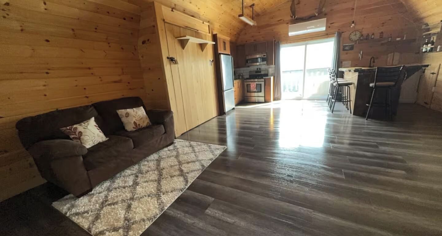 A wooden interior with a sofa, a rug, and a kitchen area.