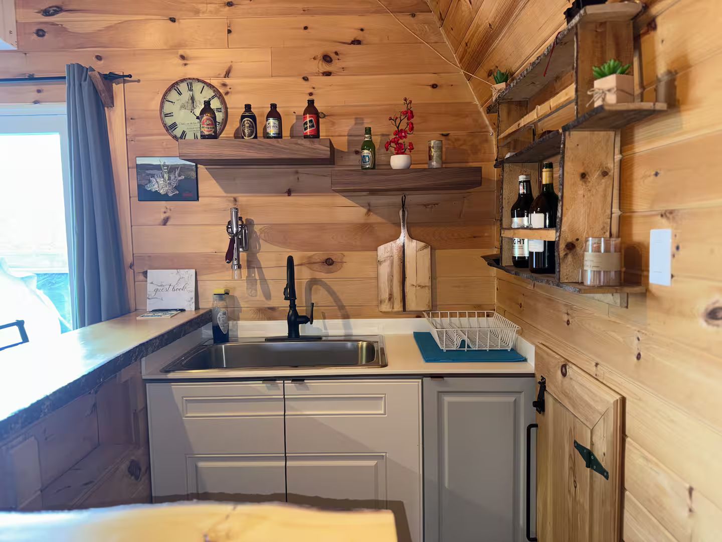 Un intérieur en bois avec un coin cuisine comprenant un évier, des placards et une horloge.