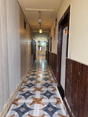 A hallway with patterned flooring, doors on both sides, and a hanging light fixture. - Hotel Max Apple In (Agra)