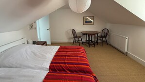 A bedroom with a bed, a dining table with chairs, a radiator, and a hanging light fixture. - Welcome to the The Old Manse, Horton, newly refurbished, meticulously designed. (Swansea)