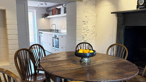 A dining area with a round wooden table surrounded by six chairs, a bowl of fruit on the table, and a hanging light fixture above. - Welcome to the The Old Manse, Horton, newly refurbished, meticulously designed. (Swansea)
