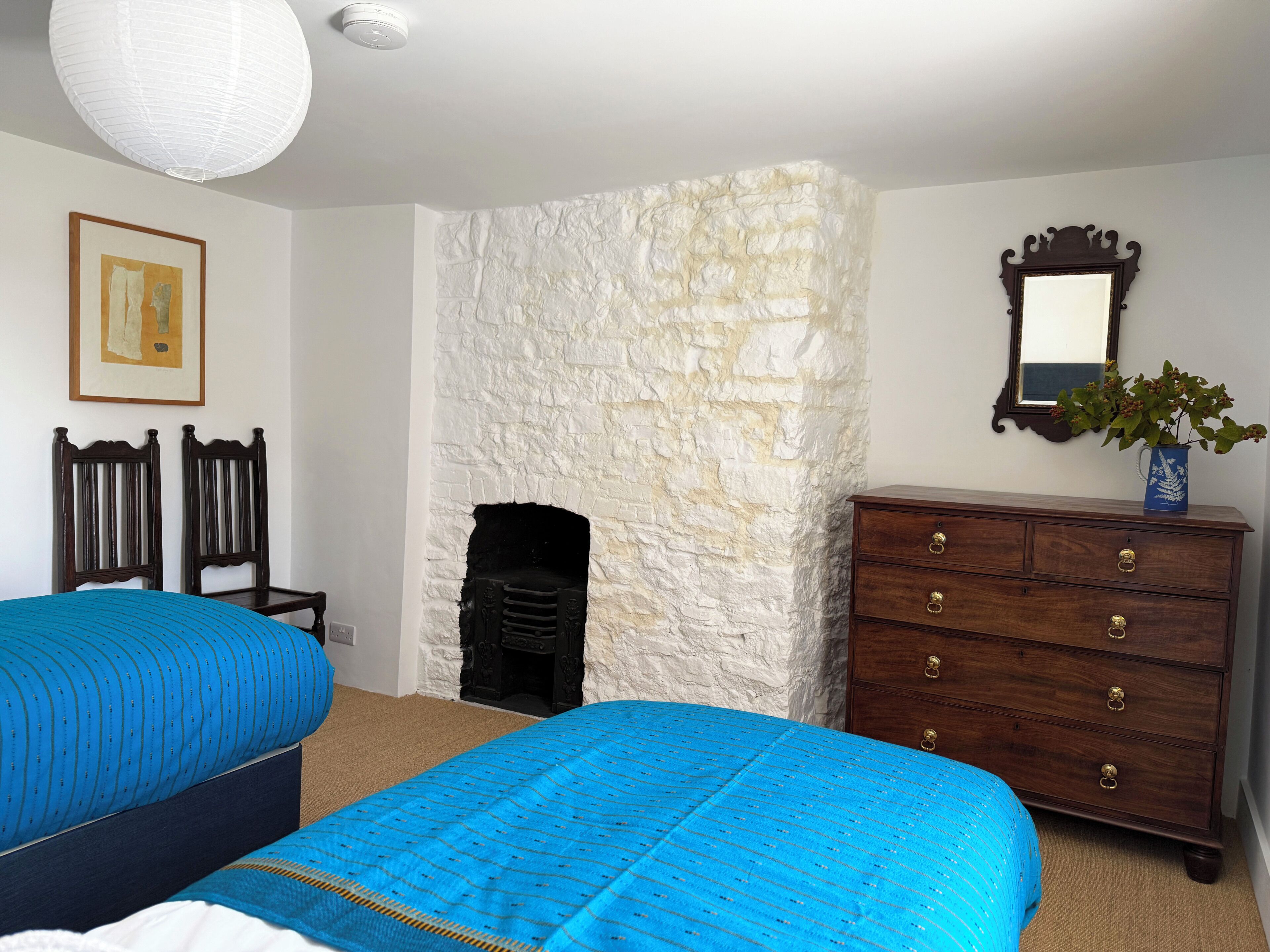 A bedroom with two beds, a dresser, a fireplace, and a mirror.