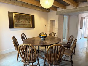 A dining area with a round table, six wooden chairs, a bowl of fruit, and a framed painting on the wall. - The Old Manse, newly refurbished, 4 bedrooms, woodburner, 5 mins from the beach (Swansea)