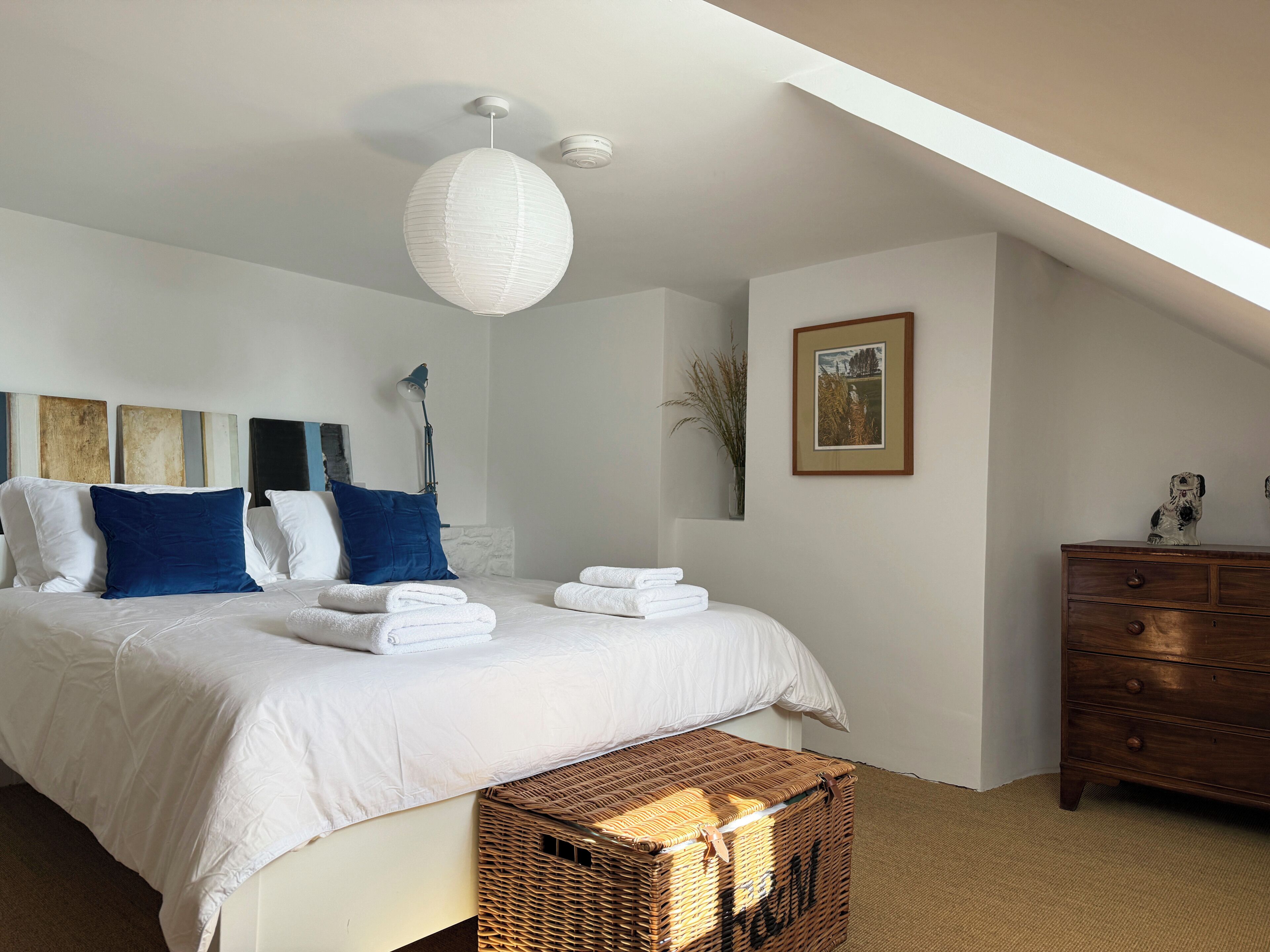 A bedroom with a bed, pillows, a dresser, a lamp, and a framed picture on the wall.