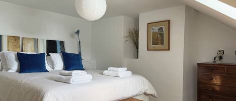 A bedroom with a bed, pillows, a dresser, a lamp, and a framed picture on the wall.
