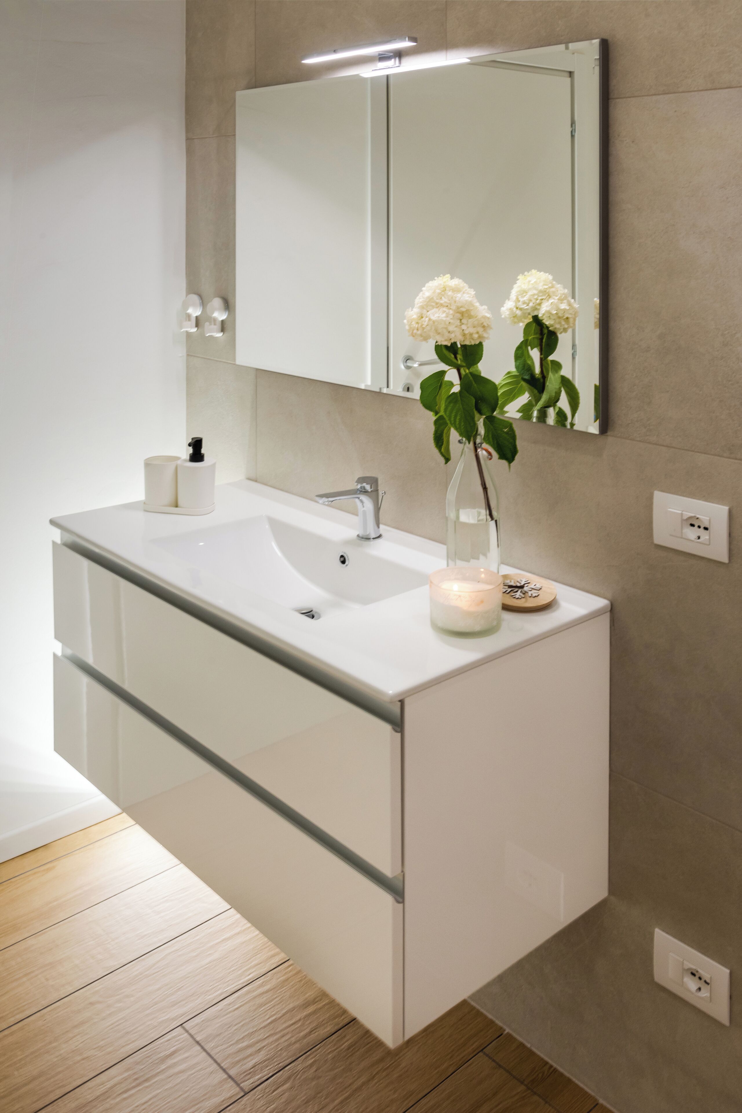 A modern bathroom with a white vanity, a mirror, and a vase with flowers.