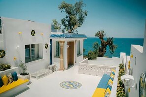 A white building with a blue roof, a small porch, and a view of the sea. - Sandra 14 (Marsa)