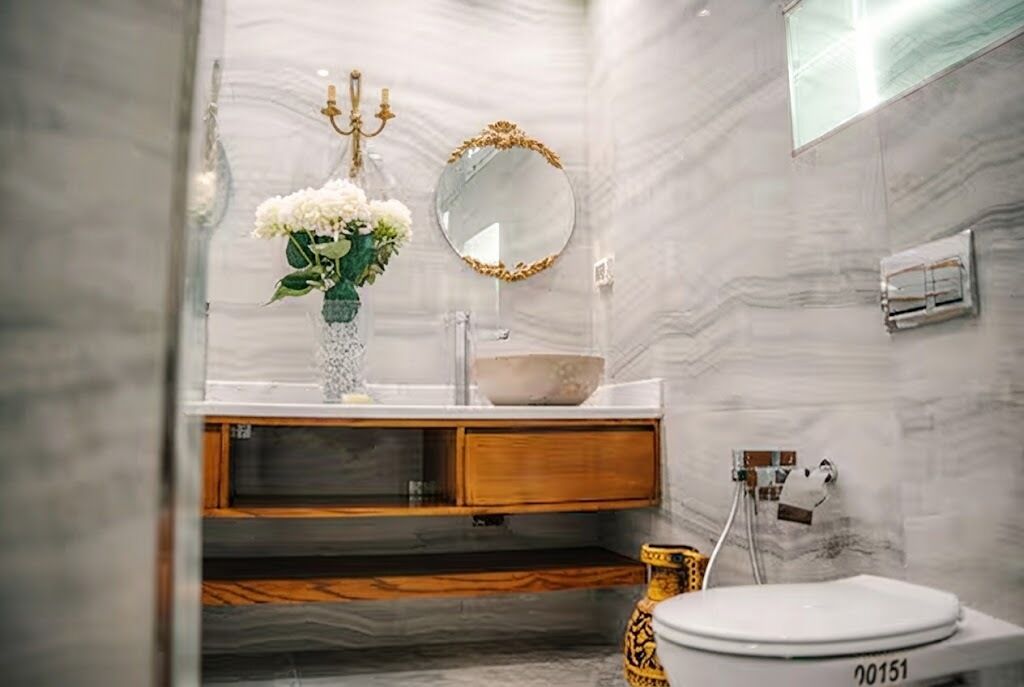 A bathroom with a marble wall, a sink with a bowl, a toilet, and a mirror with a gold frame.