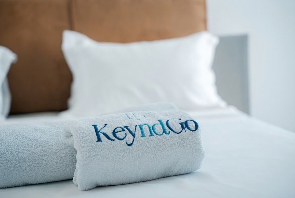 Una cama bien hecha con una toalla blanca y un almohadón con el texto 'KeyndGo'.