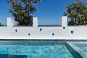 Una piscina con agua azul cristalina, rodeada de muros blancos y árboles.
