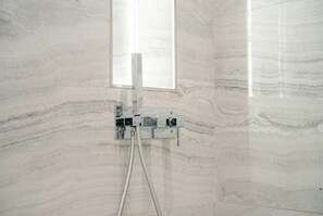 A bathroom with a marble wall, a shower with a control panel, and a window. - Sandra 14 (Marsa)