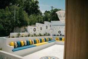 Un espacio al aire libre moderno con asientos, paredes blancas escalonadas y cojines amarillos y azules.