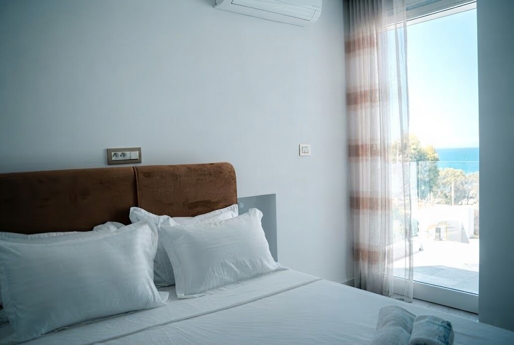 Ein Hotelzimmer mit Bett, Kopfstütze, einem Fenster mit Vorhängen und Blick ins Freie.