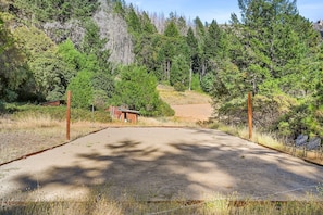 A paved entrance with a metal gate, surrounded by dense forest and a small building with a red roof. - Calistoga Retreat | Family Friendly + Private Pool (Calistoga)