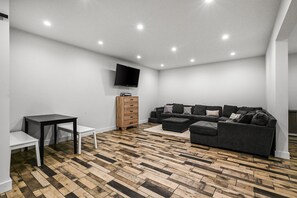 A modern living room with a sectional sofa, a flat-screen TV mounted on the wall, and a herringbone-patterned wooden floor. - Calistoga Retreat | Family Friendly + Private Pool (Calistoga)