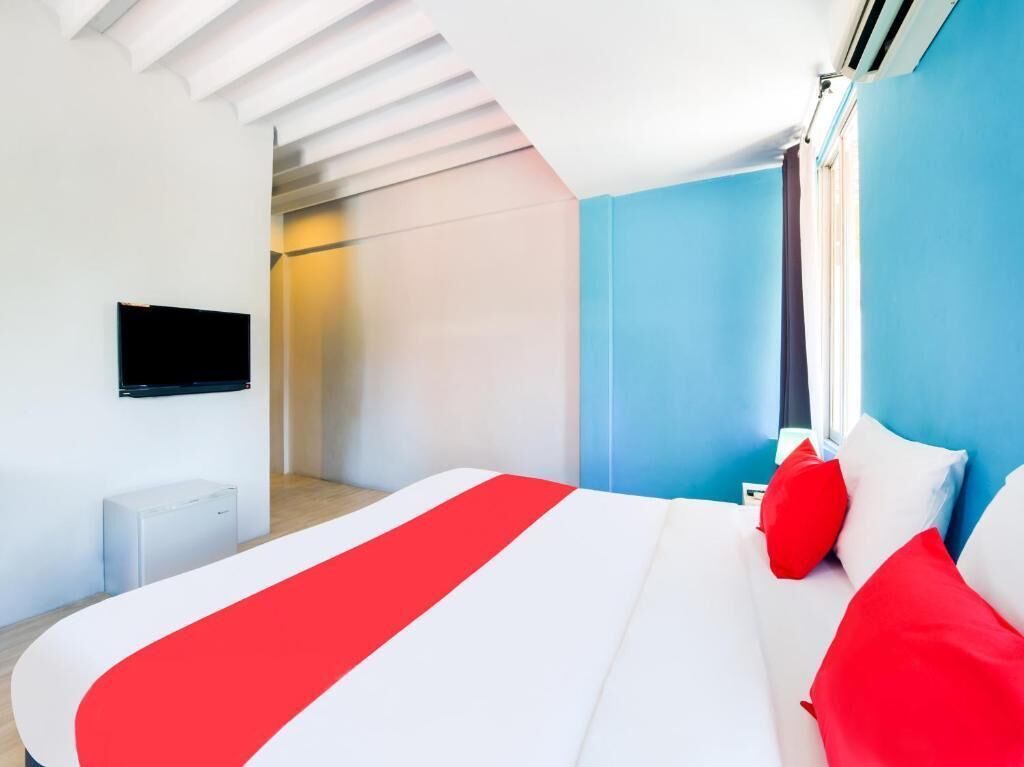 A modern hotel room with a large bed, a flat-screen TV mounted on the wall, and a window with curtains.