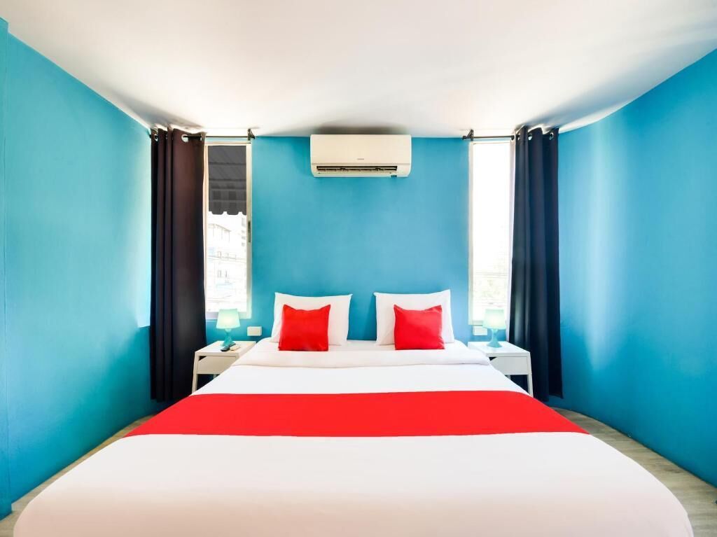 A hotel room with a bed, a nightstand, an air conditioning unit, and curtains.