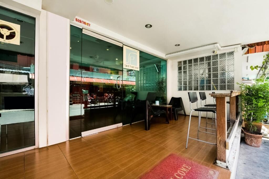A hotel lobby with a glass door entrance, a reception desk, and a seating area with chairs and tables.